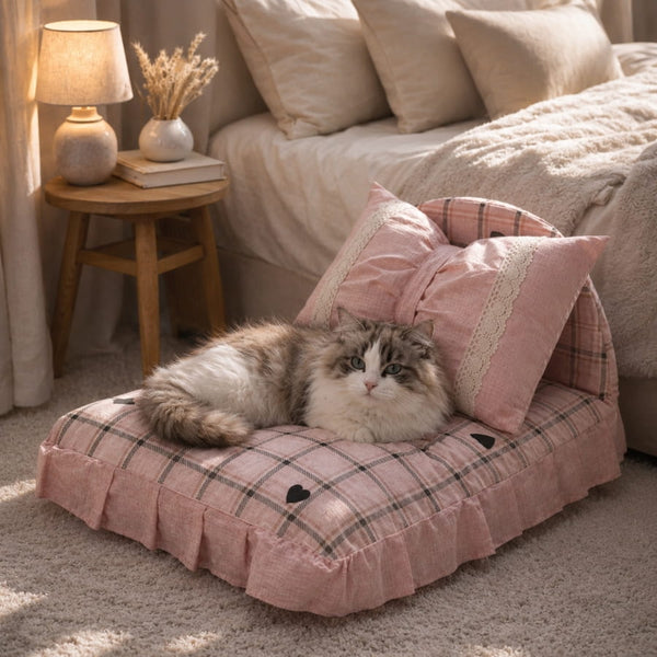 Chat à poils longs allongé sur un petit lit pour chat rose à carreaux avec coussins décoratifs, dans une chambre chaleureuse et cosy.