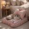 Chat à poils longs allongé sur un petit lit pour chat rose à carreaux avec coussins décoratifs, dans une chambre chaleureuse et cosy.