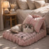 Chat à poils longs allongé sur un petit lit pour chat rose à carreaux avec coussins décoratifs, dans une chambre chaleureuse et cosy.