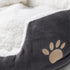 Gros plan sur la texture douce d’un petit panier pour chat gris avec intérieur moelleux blanc et motif patte brodé beige.