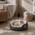Petit panier pour chat gris et blanc en peluche douce avec chat allongé, posé dans une salle de bain chaleureuse et apaisante.
