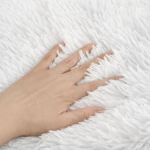 Gros plan sur la texture en fausse fourrure blanche du tapis apaisant pour chat, avec une main montrant le moelleux.