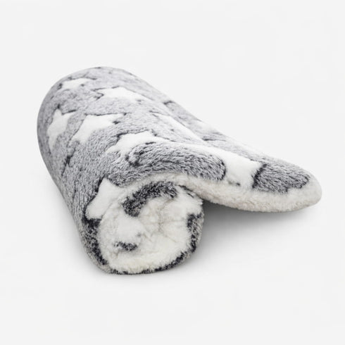 Tapis chauffant pour chat en peluche grise avec motifs étoiles blanches, roulé sur fond studio clair dans un style doux et chaleureux