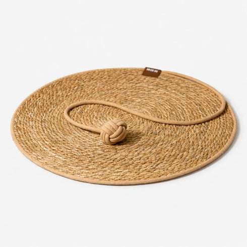 Tapis griffoir rond pour chat en fibres naturelles avec corde et balle intégrées sur fond studio clair et minimaliste