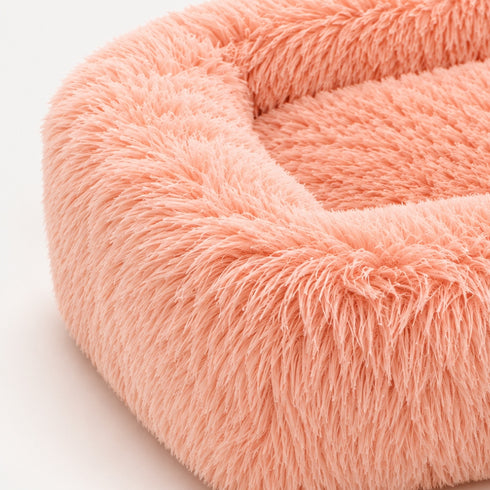 Gros plan sur la texture ultra douce et moelleuse d’un coussin apaisant rose pour chat, avec fibres longues et effet cocooning.